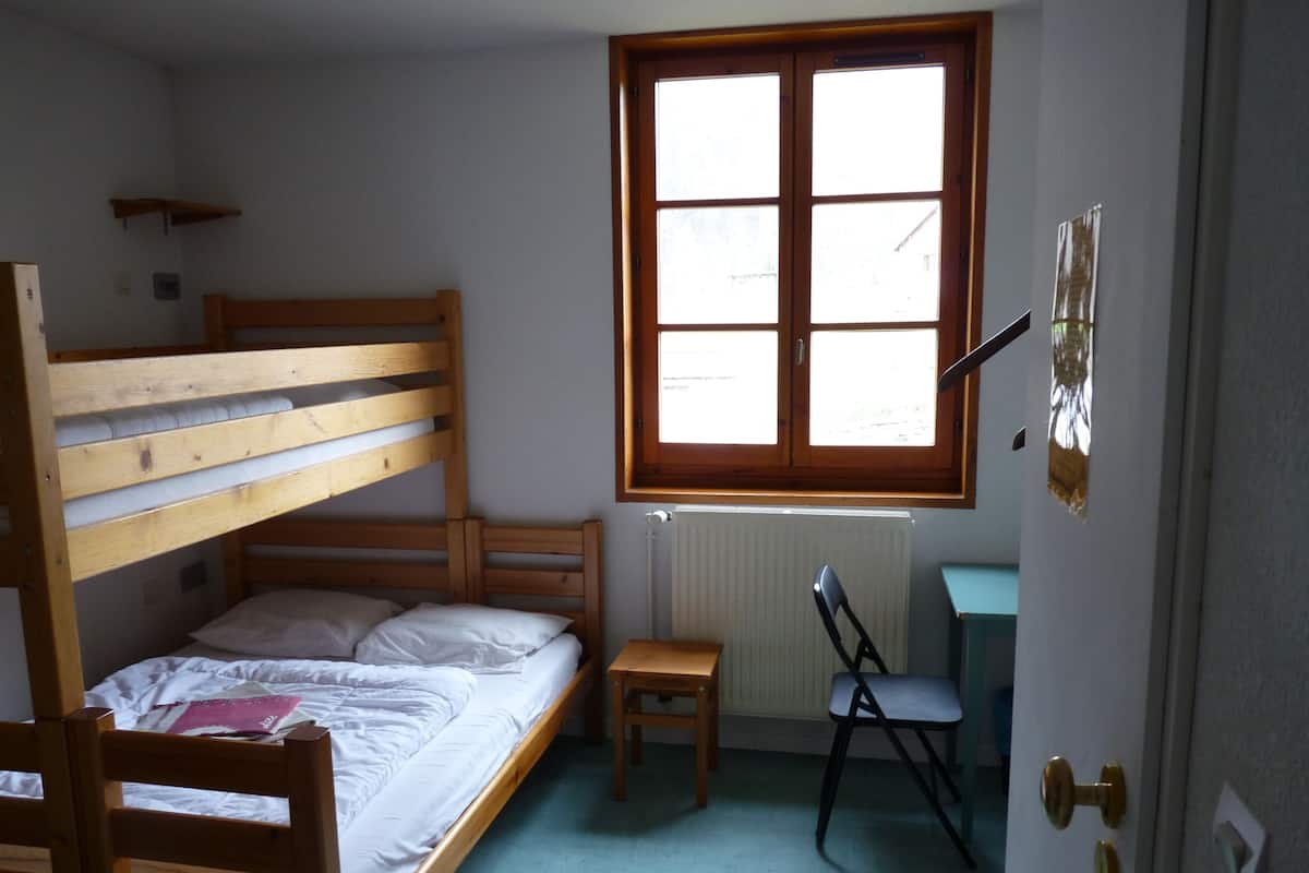 A small, sparsely furnished room with a bunk bed, a desk, and a chair.