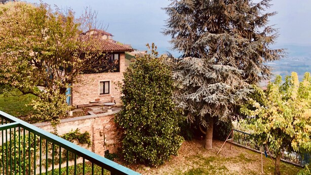 Una casa de pedra amb teulada ceràmica, envoltada de vegetació abundant i un gran arbre de fulles perennes.