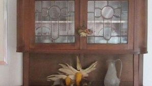 Un moble de fusta amb dues portes de vidre, una composició decorativa de flors seques i una gerra a la part superior.
