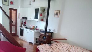 Un saló amb un sofà, dos seients còmodes, una taula de centre i una zona de cuina al fons.