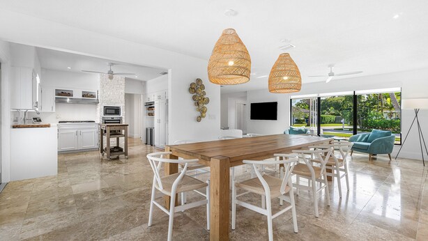 A modern kitchen with white cabinetry, a wooden dining table, and white chairs. There is a large window with a view of greenery outside. - Yacht Harbor Oasis: Beach Bliss with Private Pool  (West Palm Beach)