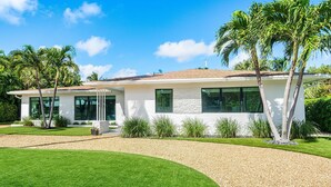 A modern house with a well-maintained lawn, palm trees, and a clear blue sky. - Yacht Harbor Oasis: Beach Bliss with Private Pool  (West Palm Beach)