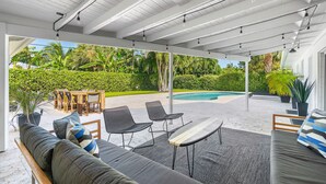 A covered outdoor seating area with a pool, chairs, and a sofa. - Yacht Harbor Oasis: Beach Bliss with Private Pool  (West Palm Beach)