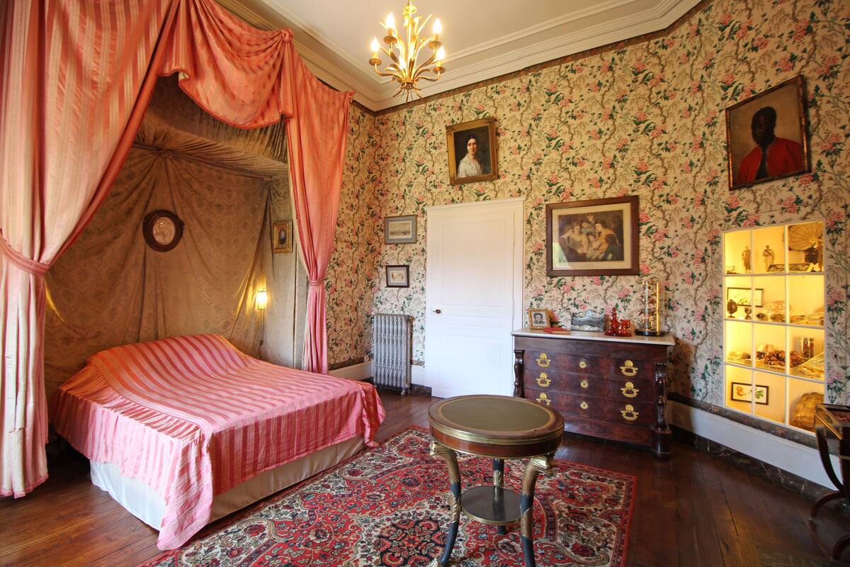 Ein Schlafzimmer mit Baldachinbett, Kommode und kleinem Tisch.