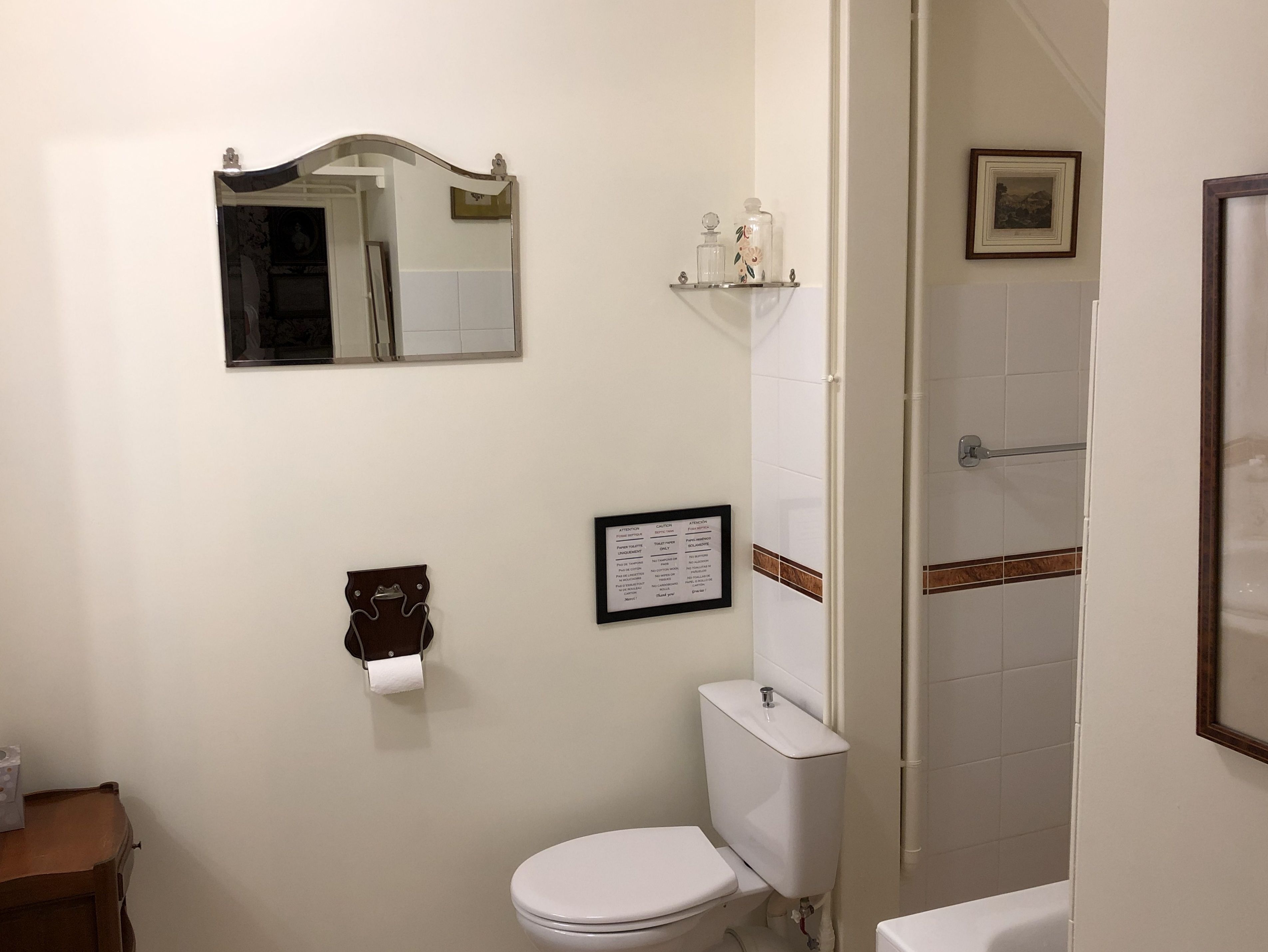 A bathroom with a toilet, a sink, a mirror, a framed sign, and a shower area.