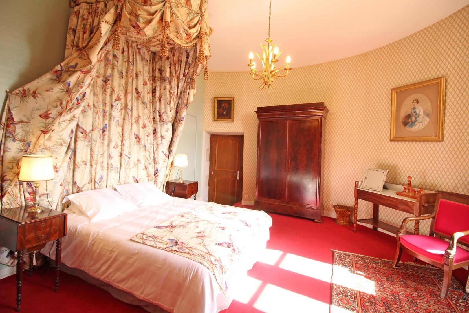 A bedroom with a large bed, a wooden wardrobe, a desk with a chair, and a chandelier.