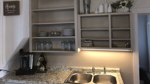 Une cuisine dotée de plans de travail en granit, d’éviers en acier inoxydable et d’une étagère intégrée où sont rangés la verrerie et la vaisselle.