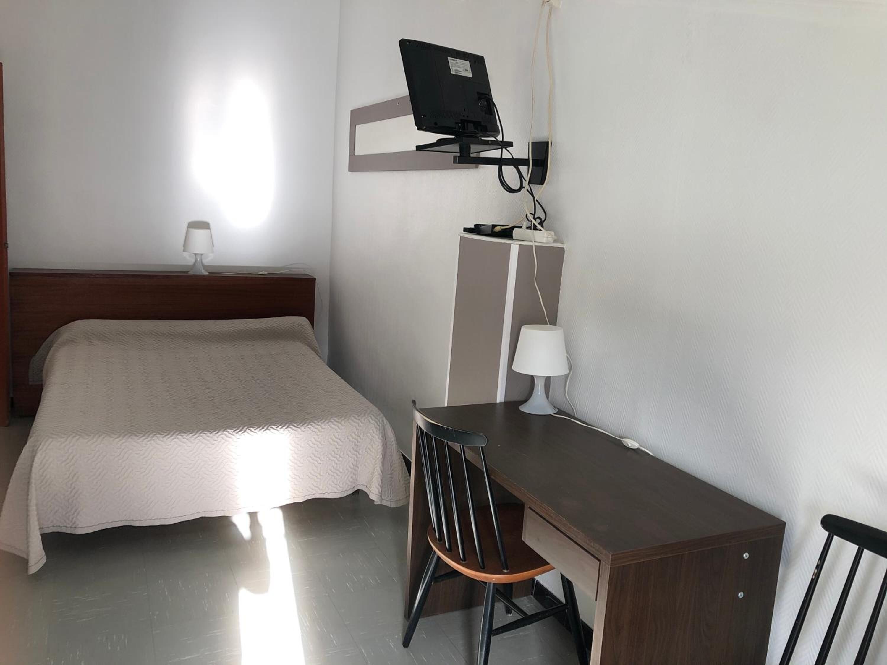 Hotelkamer met een bed, een bureau, een stoel, een aan de muur bevestigde televisie en een lamp op het bureau.