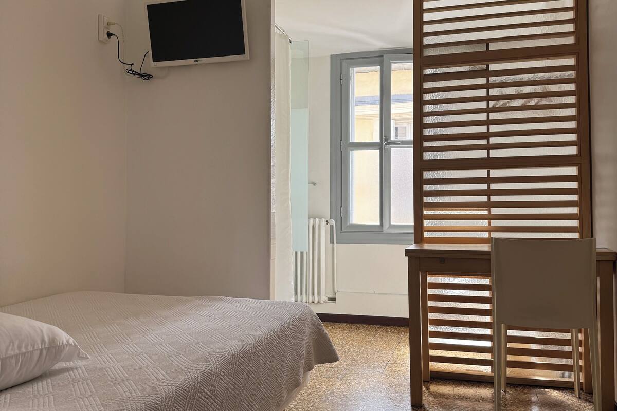 A bedroom with a bed, a desk, and a TV mounted on the wall.