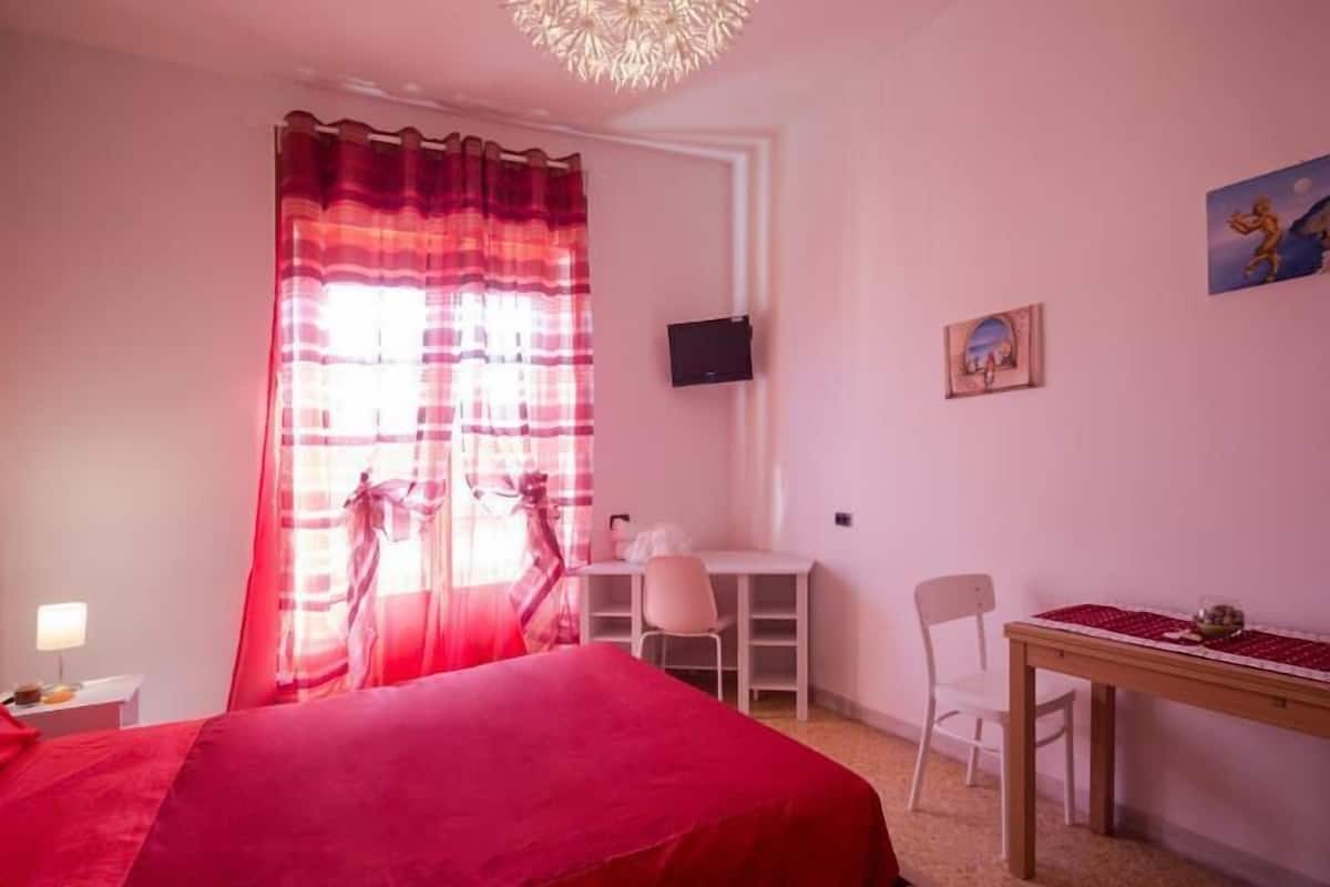 Ein Schlafzimmer mit einem Bett, einem Schreibtisch, einem Stuhl und einem an der Wand befestigten Fernseher.