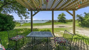 A covered patio with a table and chairs, overlooking a body of water and a distant bridge.
