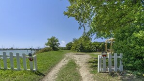 A dirt path leading to a wooden gazebo with a white picket fence on either side.