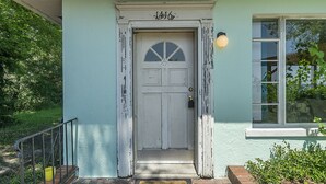 A white door with a small window above it, a light fixture on the wall to the right, and a yellow bucket on the steps.
