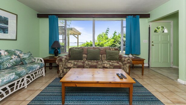 A living room with a sofa, a coffee table, and a TV. There is a window with curtains, a door, and a framed picture on the wall.