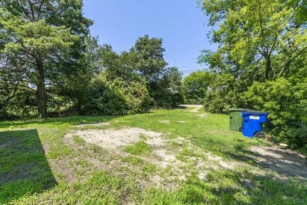 A grassy area with a dirt path, surrounded by trees and two green dumpsters.