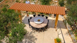 An outdoor patio with a round table and chairs, surrounded by a pergola with a corrugated metal roof. - Castell des Paradís - Family villa near the sea (Portopetro)