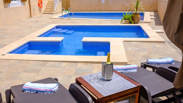 A pool area with two separate pools, lounge chairs, a table with a bottle of champagne, and potted plants. - Castell des Paradís - Family villa near the sea (Portopetro)