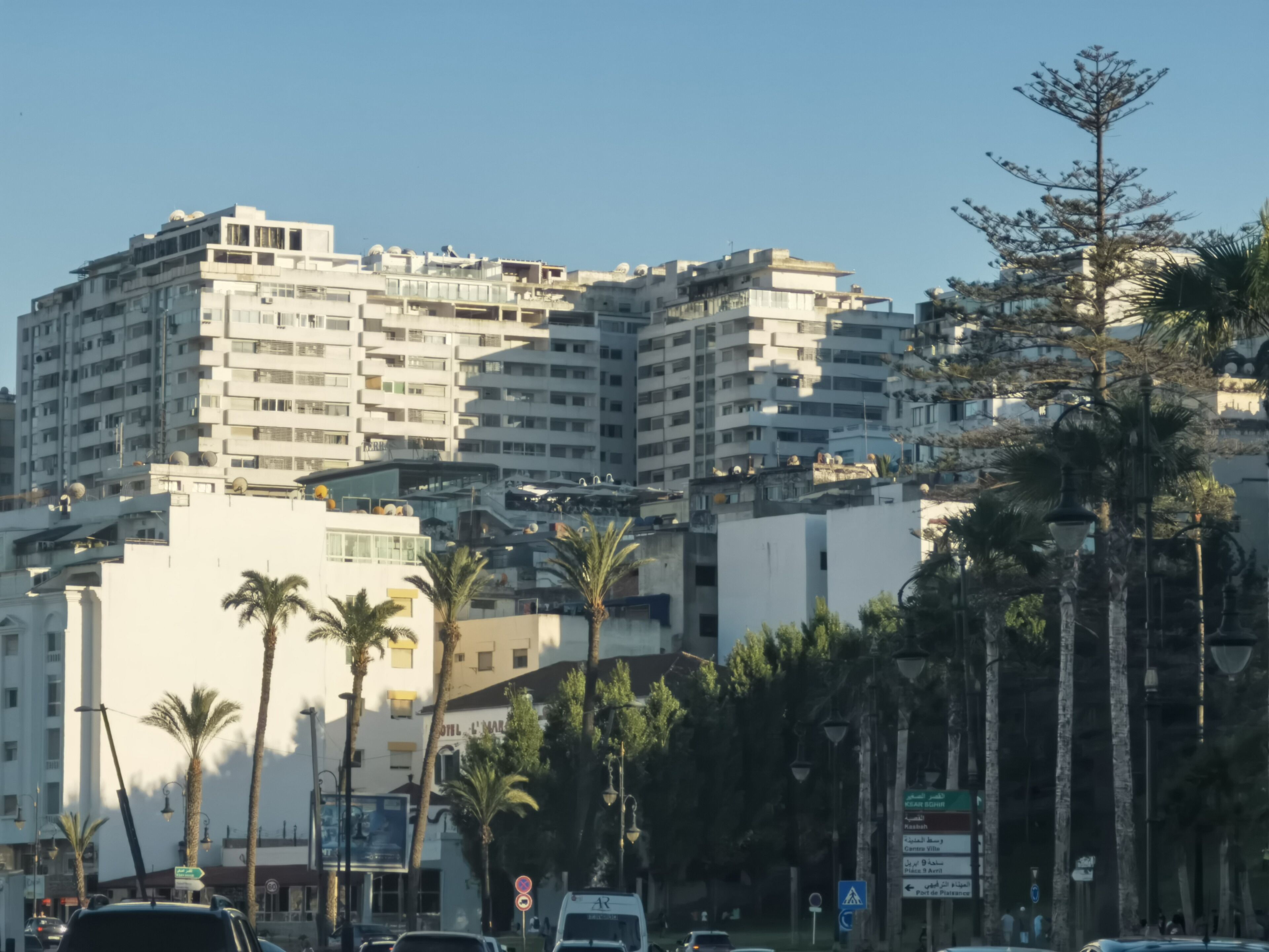 A multi-story building with balconies, palm trees, and street signs.