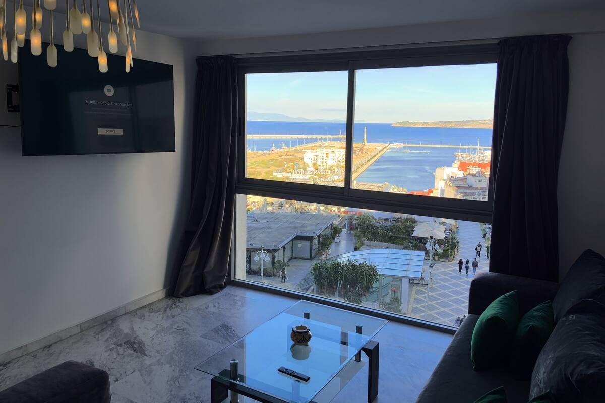 A modern living room with a large window offering a view of a coastal cityscape.