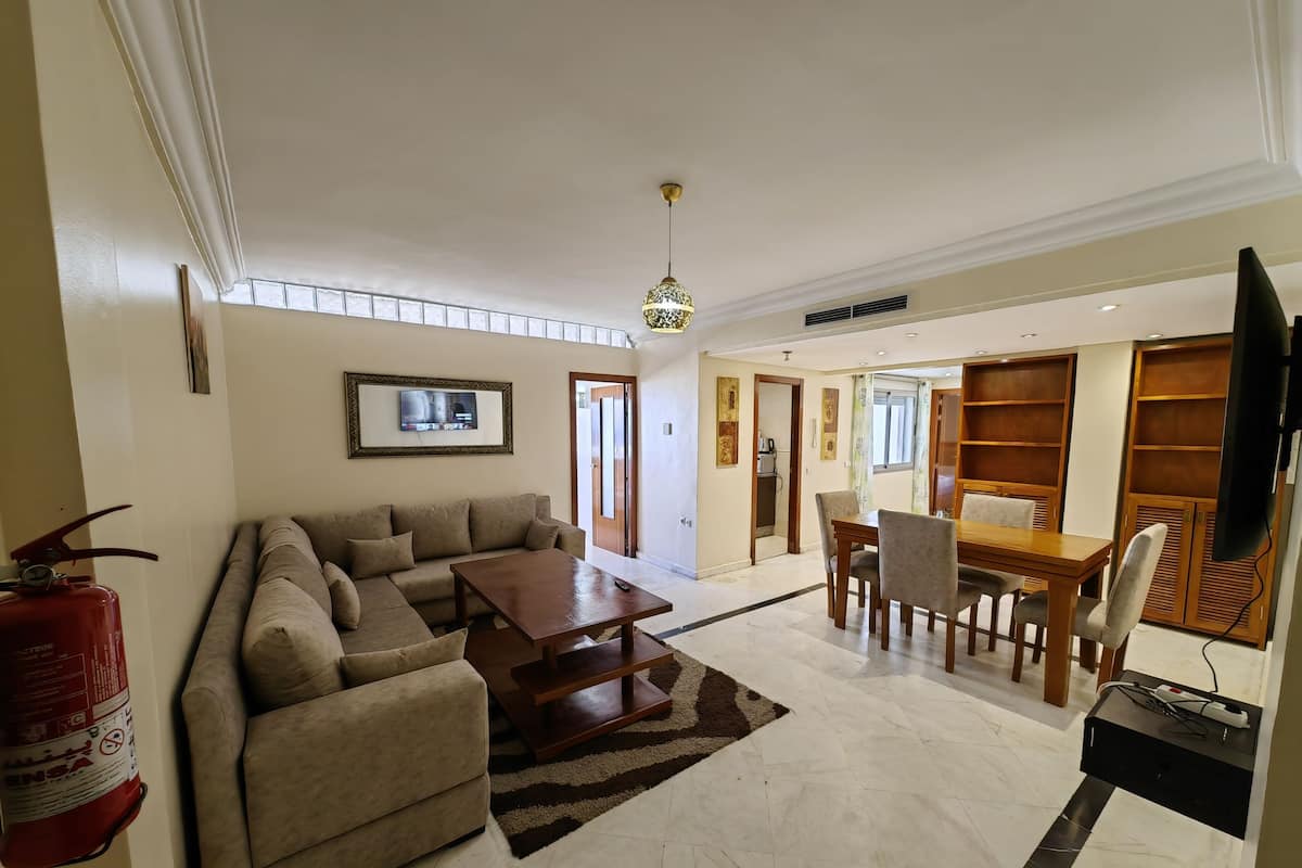 A spacious living room with a sofa, coffee table, and dining area. A fire extinguisher is mounted on the wall.