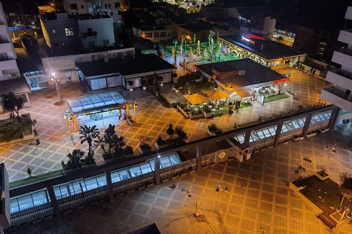 An aerial view of a plaza with a restaurant, outdoor seating, and a covered area with a sign.