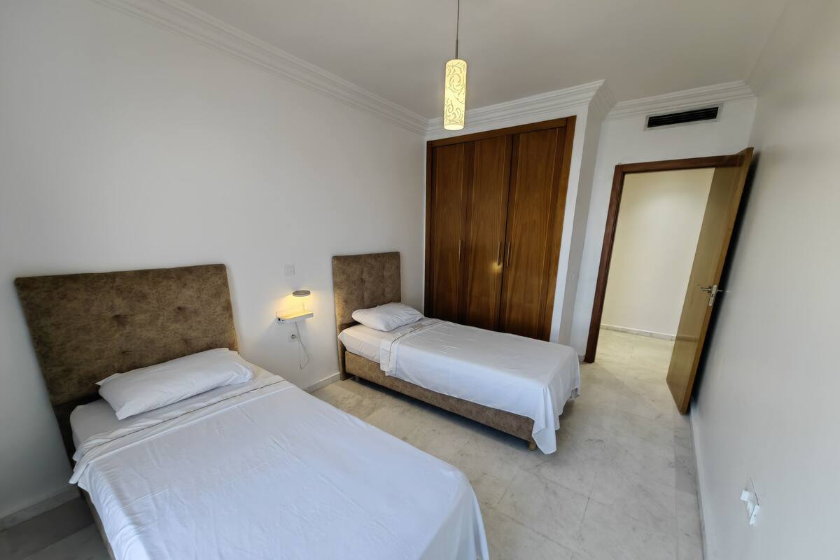 A bedroom with two beds, a wardrobe, and a pendant light.