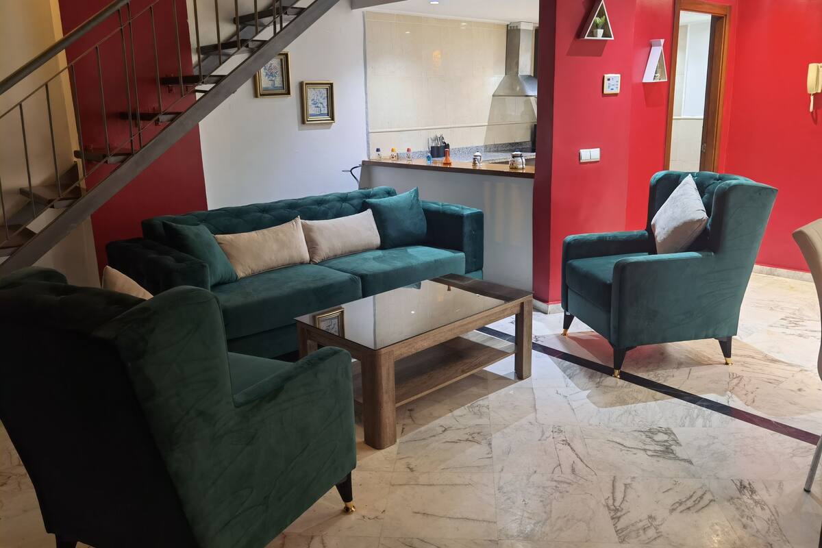 A living room with a green sofa set, a coffee table, and a staircase.