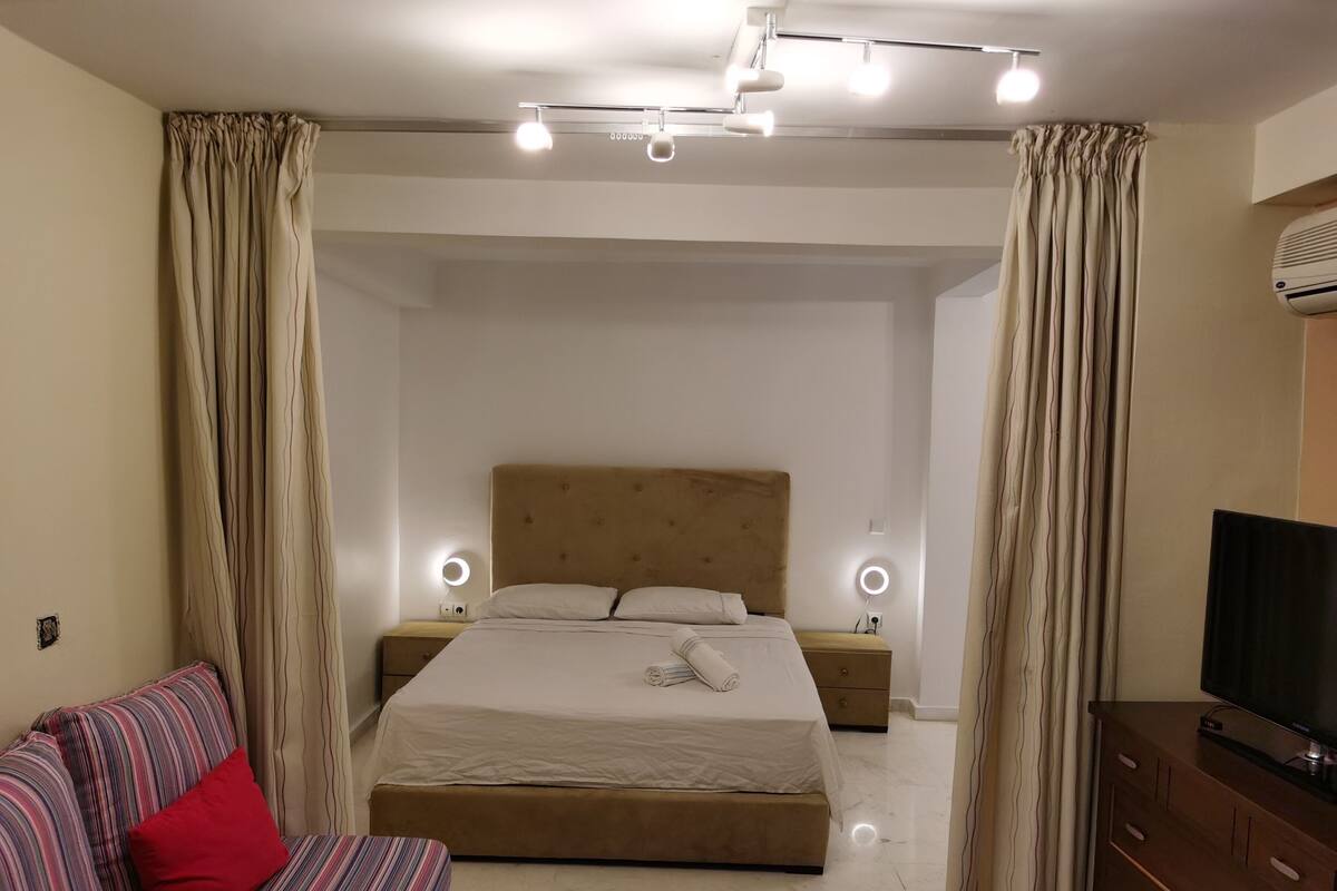 A modern bedroom with a large bed, bedside lamps, a TV, and a sofa.