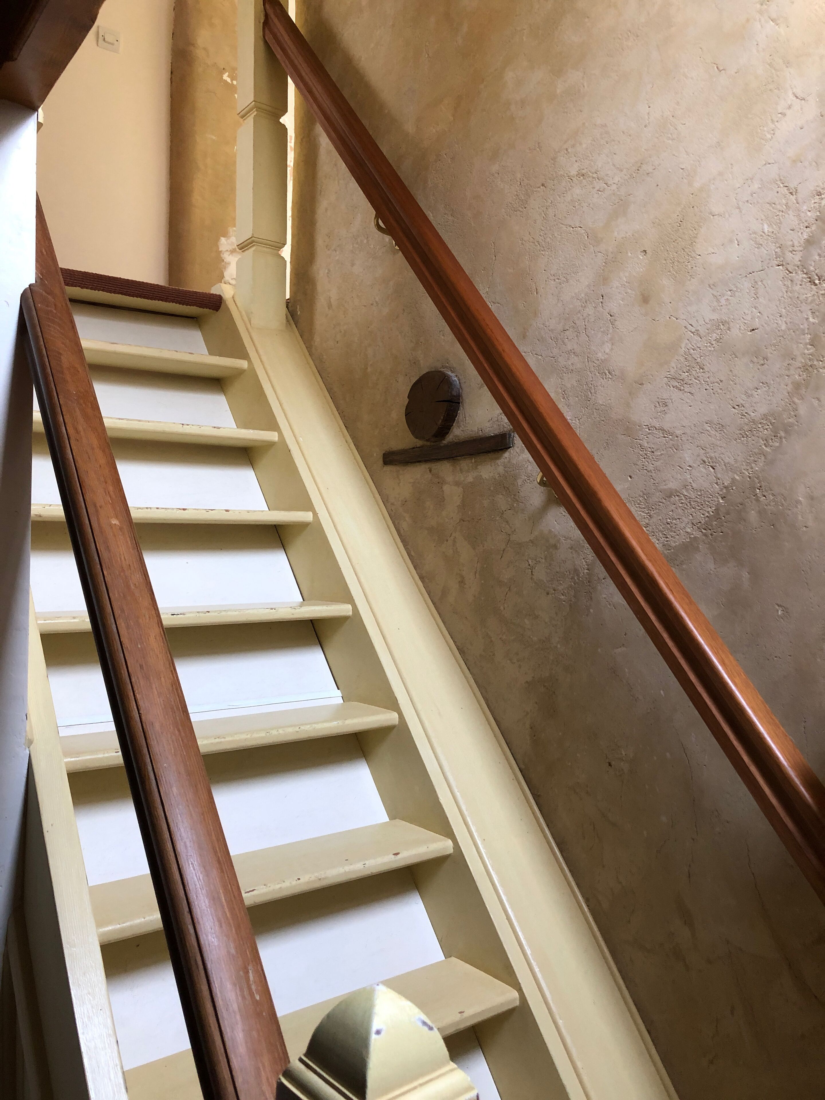 A staircase with wooden handrails and white steps, leading to a landing with a small round table and a wall-mounted shelf.