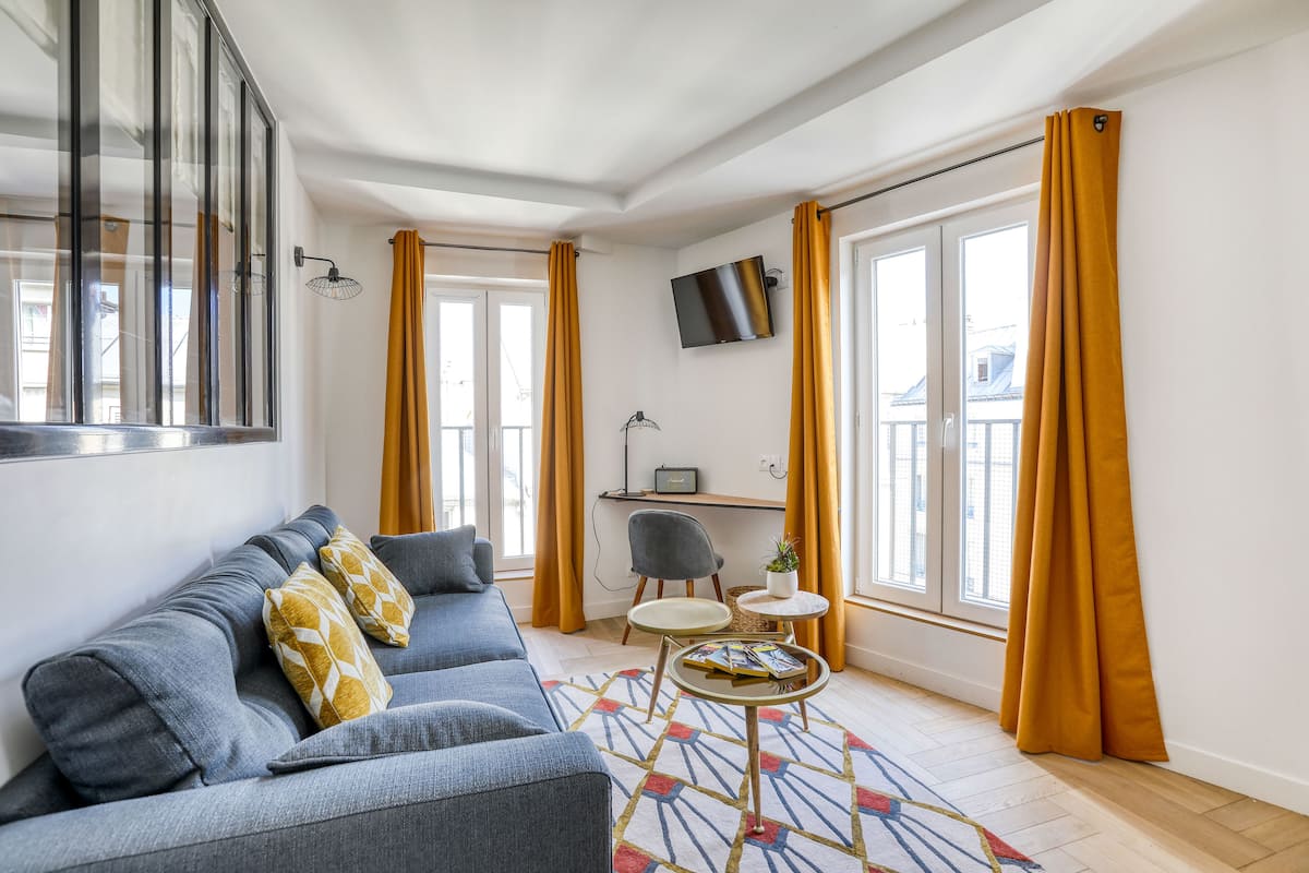 Un salon moderne avec un canapé gris, une petite table ronde et un téléviseur fixé au mur.
