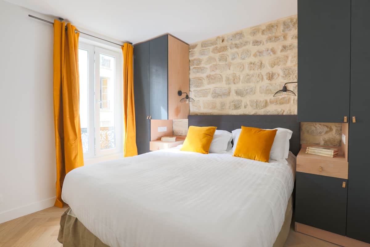 Une chambre à coucher avec un lit, une table de chevet, une armoire et un mur en pierre.