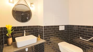 A bathroom with a white sink, a round mirror, a toilet, and black tiled walls.