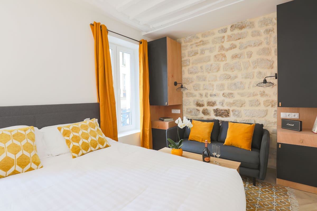 Une chambre d’hôtel avec un grand lit, un canapé, un mur en pierre et une petite table sur laquelle se trouvent une bouteille et des verres.