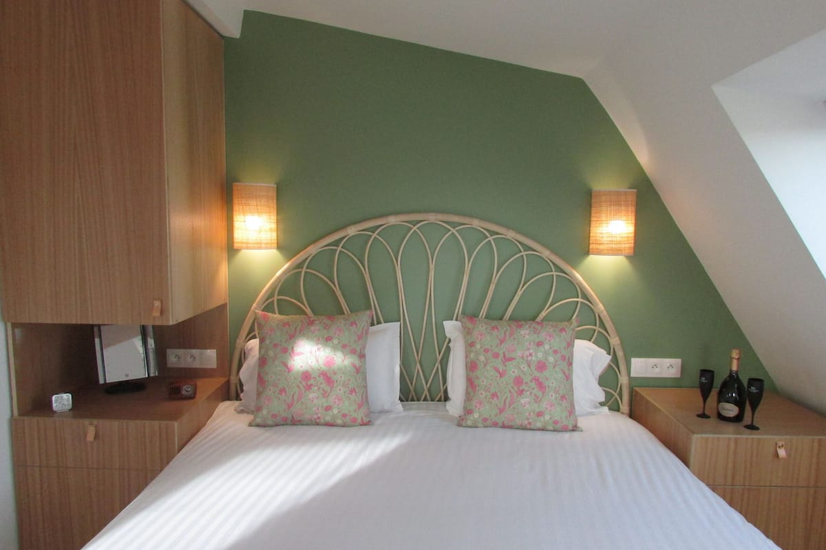 Une chambre à coucher avec une tête de lit incurvée, deux lampes de chevet, une bouteille de champagne et une petite table sur laquelle se trouvent une bouteille et des verres.