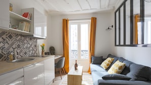 A modern living space with a kitchen, a dining area, and a seating area with a sofa and cushions. - Le Matissia (Paris)