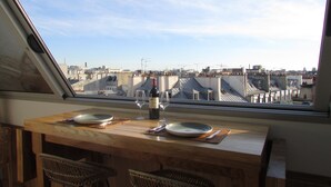 A dining area with a table set for two, a bottle of wine, and two glasses. The room has a view of a cityscape through a skylight. - Le Matissia (Paris)