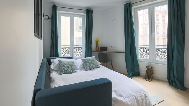 A bedroom with a bed, a desk, a chair, and a window with curtains. - Le Matissia (Paris)