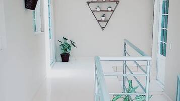 Un interior espacioso con una escalera que conduce a un comedor, una planta en maceta y estanterías fijas a la pared.