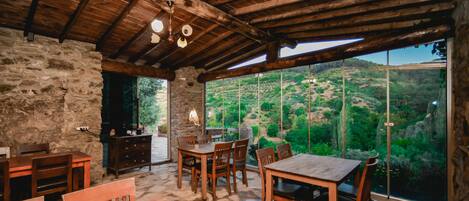 A rustic dining area with stone walls and wooden furniture, overlooking a lush valley.