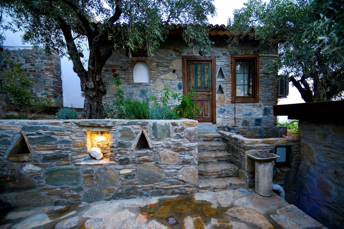 A stone building with a wooden door, a small window, and a stone wall with a light fixture.