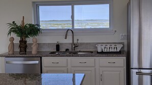 A kitchen with a granite countertop, white cabinets, a stainless steel refrigerator, and a window with a view of a water body. - Golden Surfside--It has GOLDEN VIEWS and it's brand new!! (Surfside Beach)