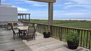 A wooden deck with a table and chairs, overlooking a grassy area and the ocean. - Golden Surfside--It has GOLDEN VIEWS and it's brand new!! (Surfside Beach)