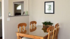 Un coin repas avec une table et des chaises en bois, un lustre, un tableau encadré et une plante accrochée au mur.