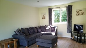 A living room with a sectional sofa, ottoman, wooden coffee table, and a TV on a stand. - Swallows Nest, Cottage, Fishing Lakes Nr Cleethorpes, Adults Only Pet Friendly  (Lincolnshire)