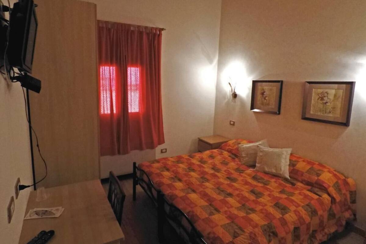 A bedroom with a bed, a desk, a chair, a TV, and a window with red curtains.