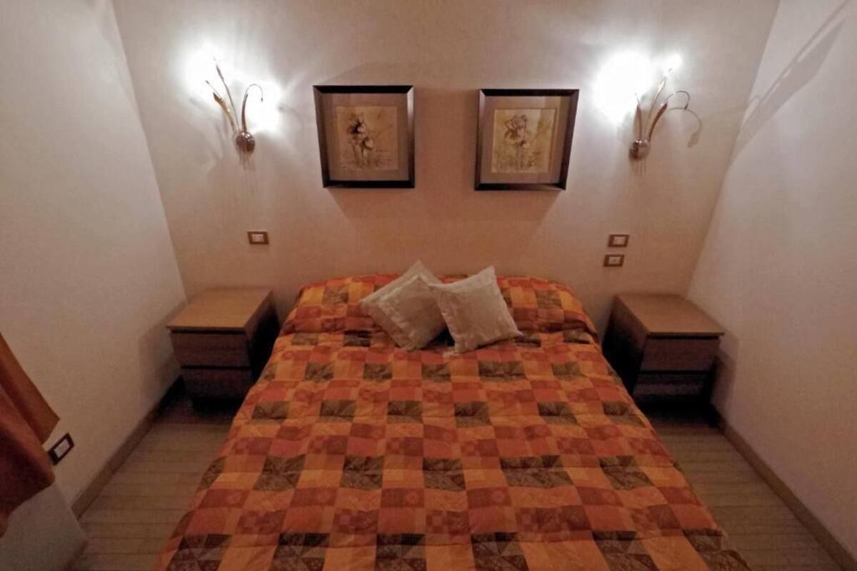 A bedroom with a checkered bedspread, two wall-mounted light fixtures, and framed artwork on the wall.