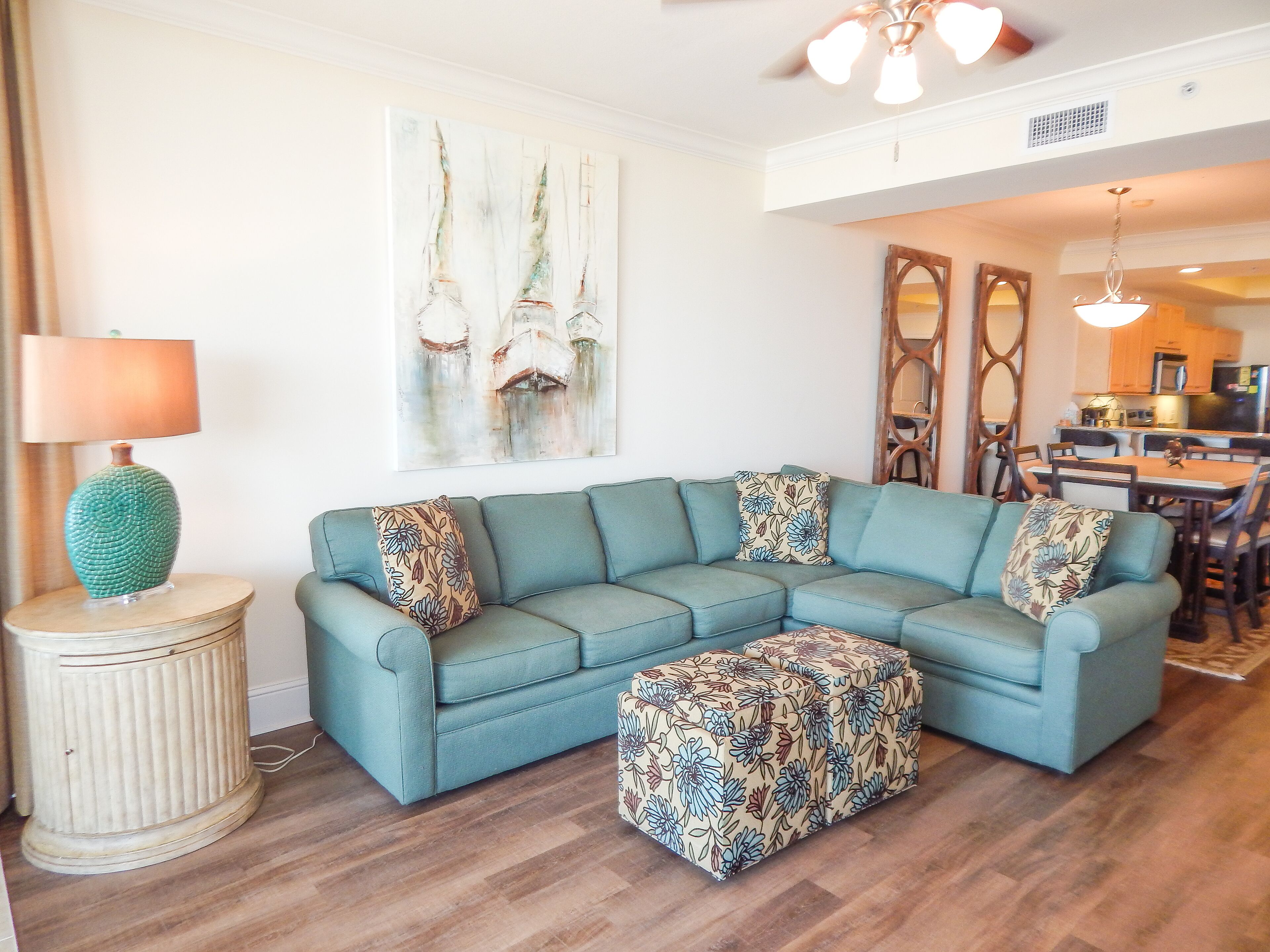 A living room with a sectional sofa, a side table with a lamp, and a floral ottoman.