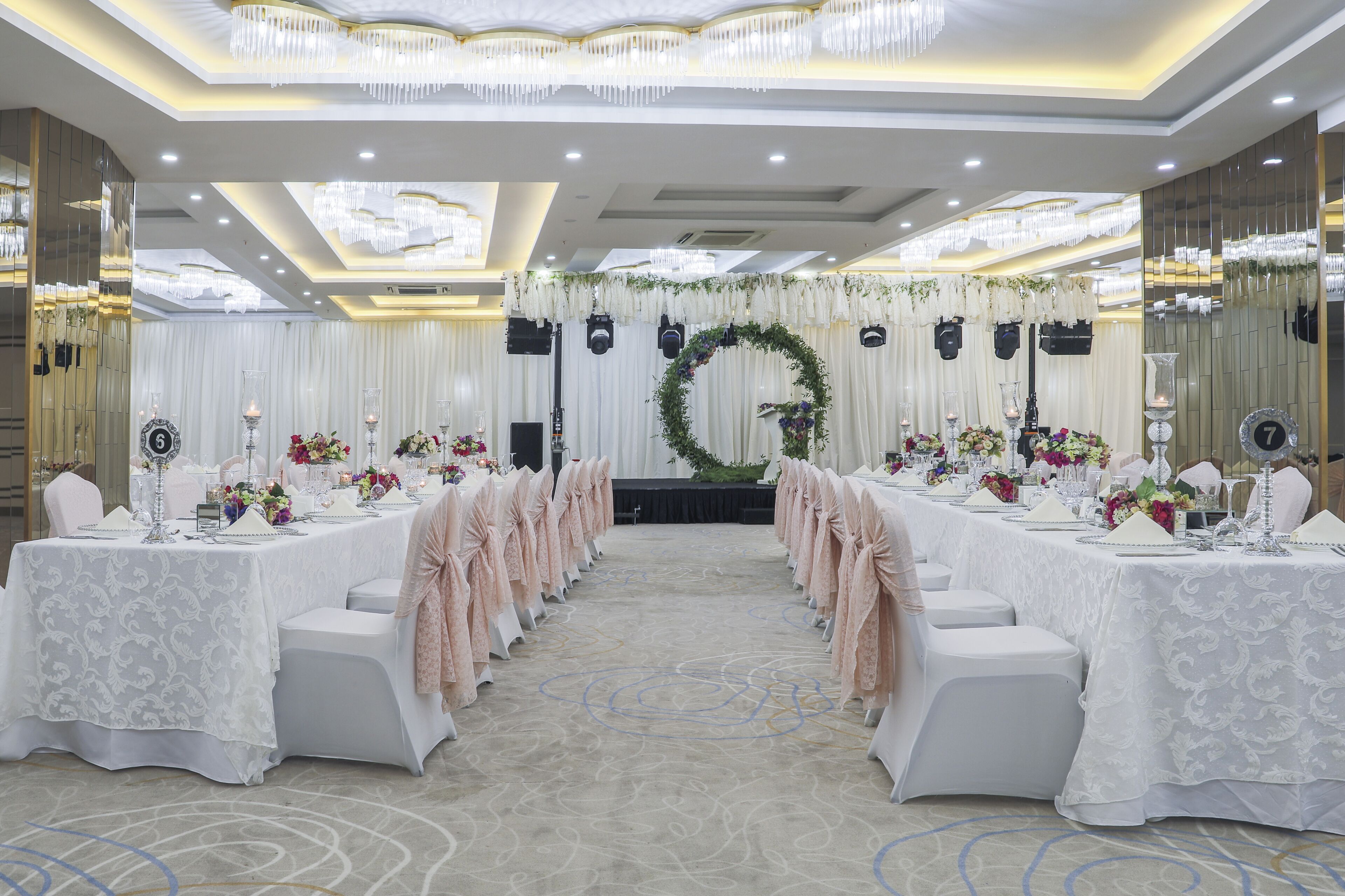 Un salón de banquetes con mesas dispuestas para un evento formal, con un arreglo floral central y una araña.