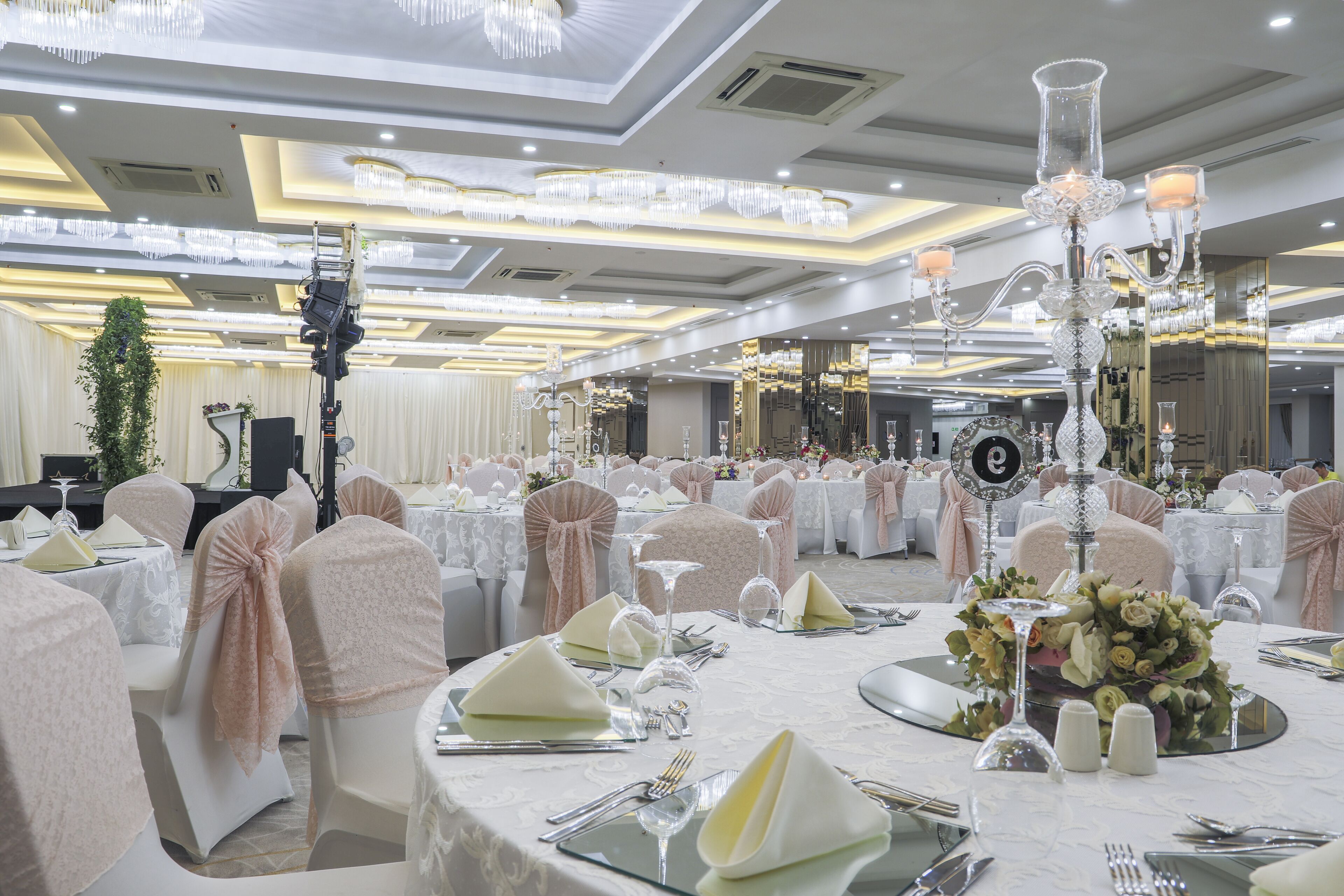 A banquet hall with round tables set for a formal event, featuring white tablecloths, glassware, and floral centerpieces.