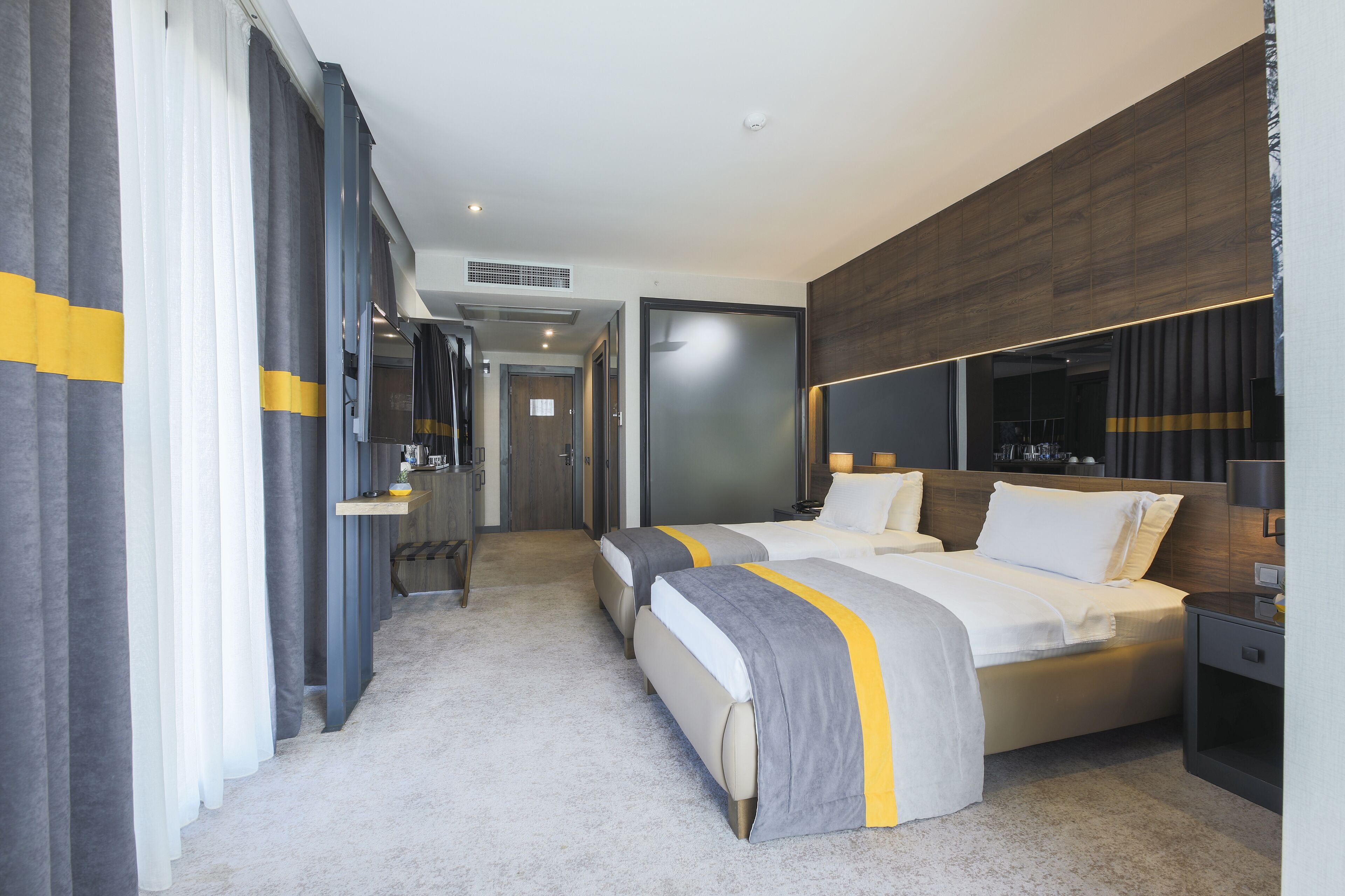 A modern hotel room with two beds, a large mirror, and a wooden accent wall.